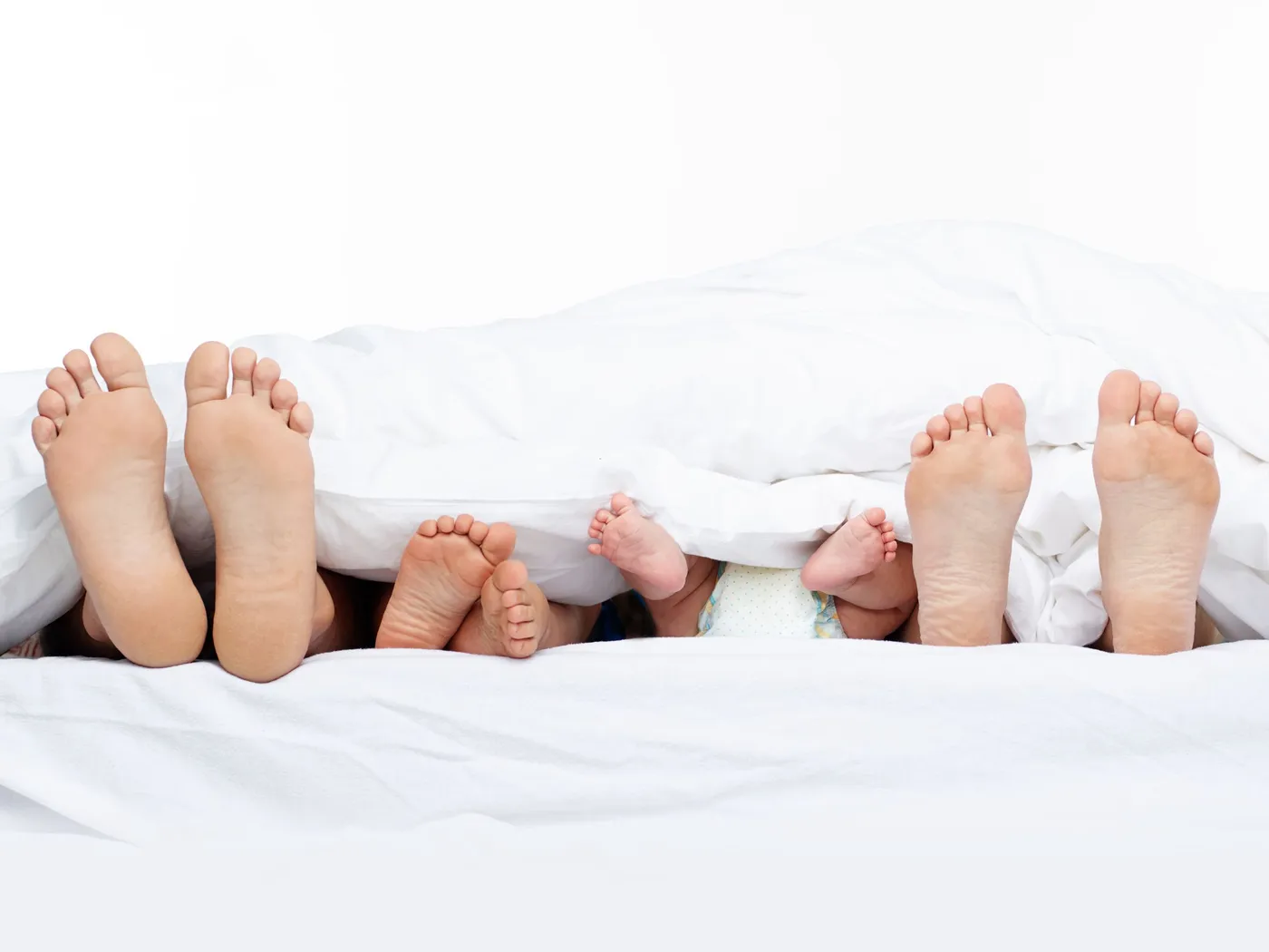 Füße von Eltern und Kindern schauen unter einer weißen Bettdecke hervor